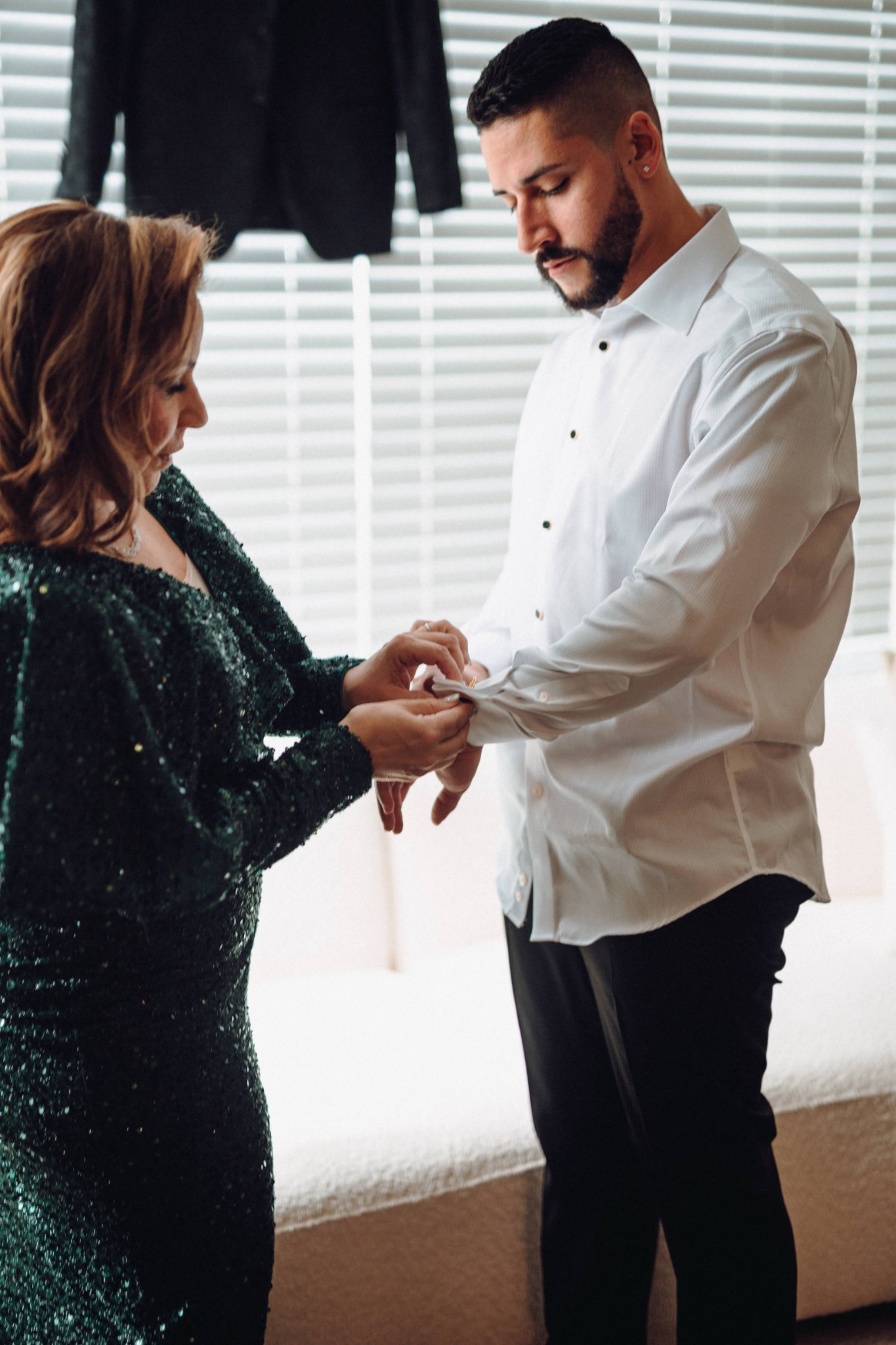 A loved one fastening the groom's cuff before the wedding
