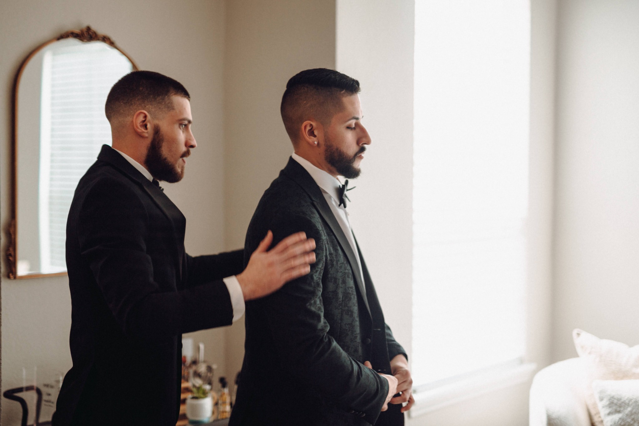 Groomsman helping the groom prepare by a bright window